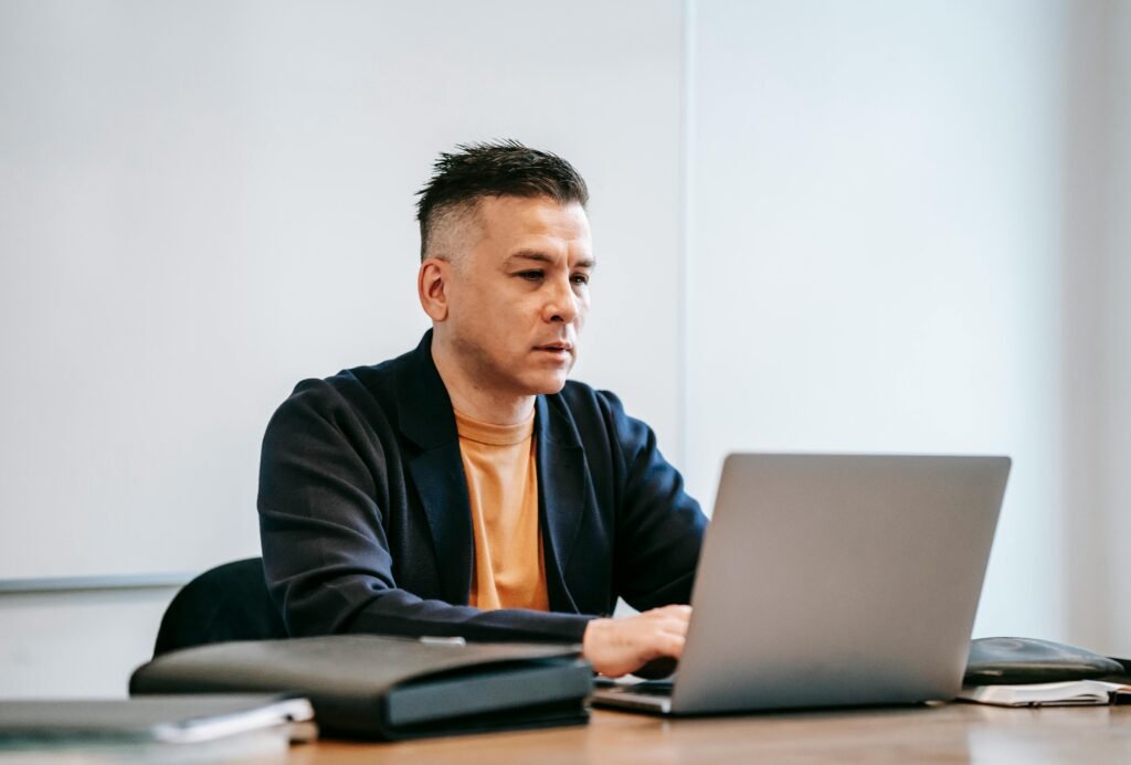 A concentrated man working remotely on his laptop in a modern indoor office setting.